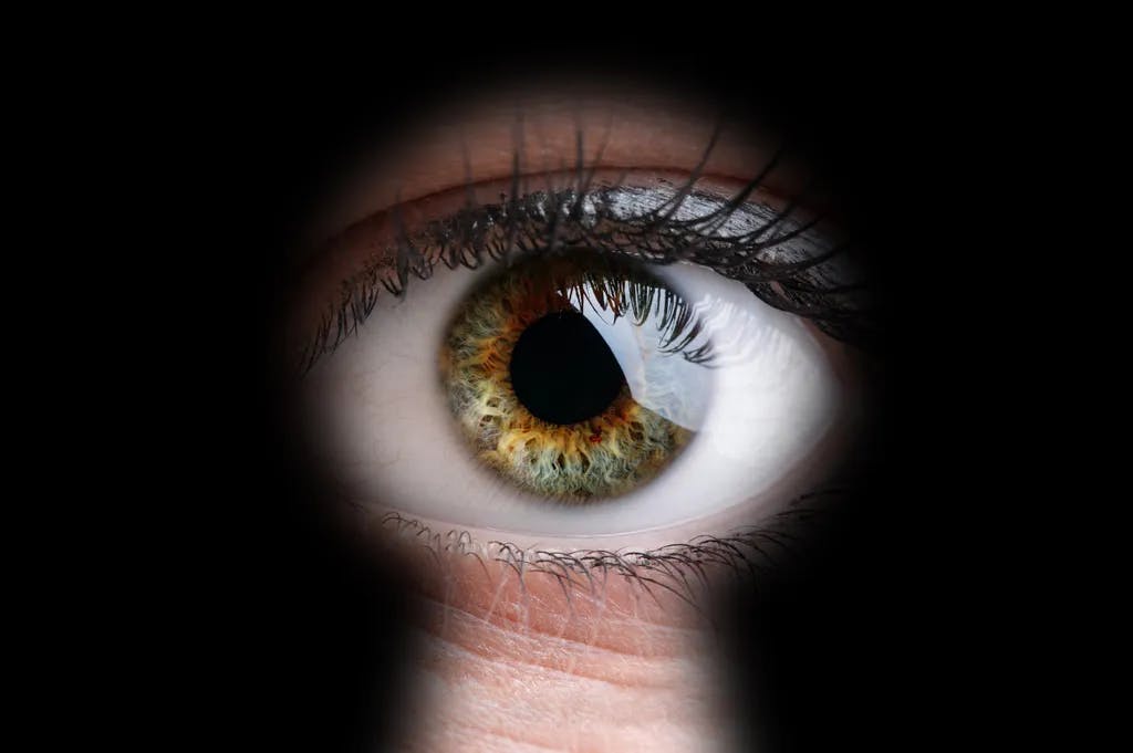 Weibliche Augen durch ein Schlüsselloch-Konzept für Neugier, Stalker, Überwachung und Sicherheit