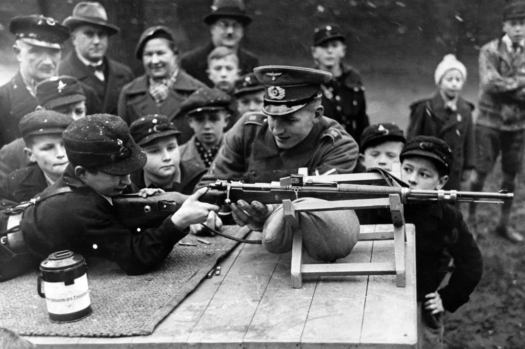 Hitlerjungen der Deutschen Jugend bei Schießübungen unter der Aufsicht eines Angehörigen der Deutschen Wehrmacht. Datum und Ort unbekannt.