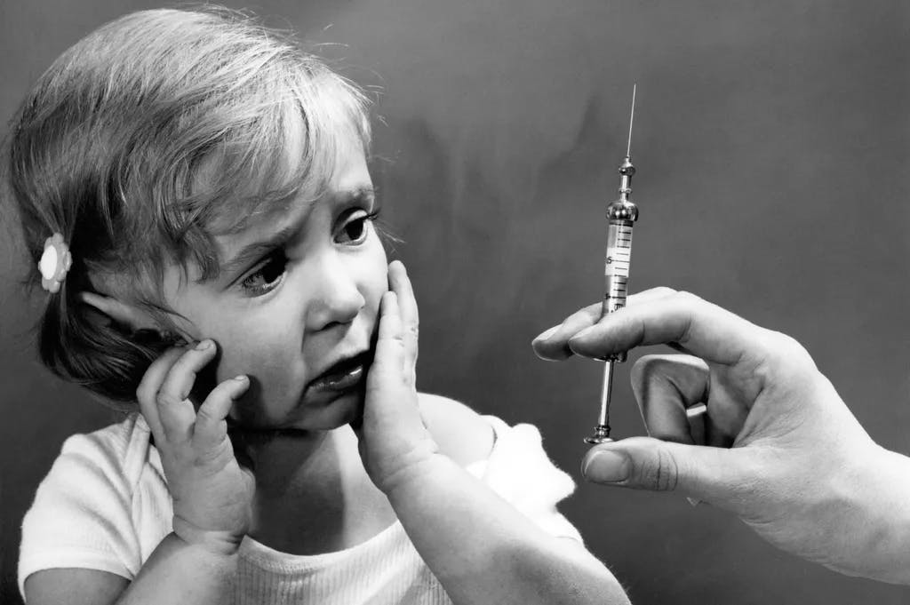 Deutschland, Impfen, kleines Mädchen blickt skeptisch zu einer aufgezogenen Spritze.